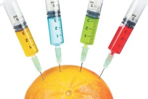 A grapefruit being injected with four syringes containing colored fluids